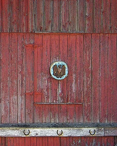 Barn with Eagle. Color photograph of an old, weathered red barn. The hay door in the middle has an old eagle plaque affixed and three rusty iron horse shoes line the white trim.